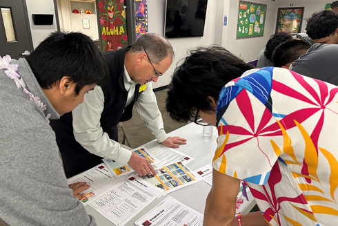 man and two teenagers looking at papers on table in classroom