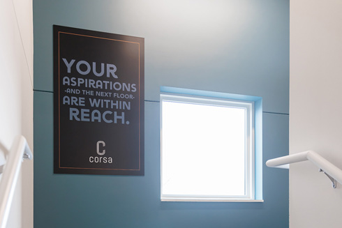 sign at the top of the stairs in apartment building reading, "Your Aspirations, and the next floors, are within reach. Corsa"