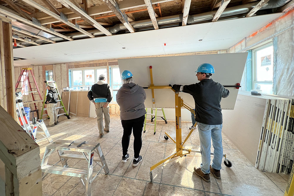 several people work on hanging drywall inside a home under construction