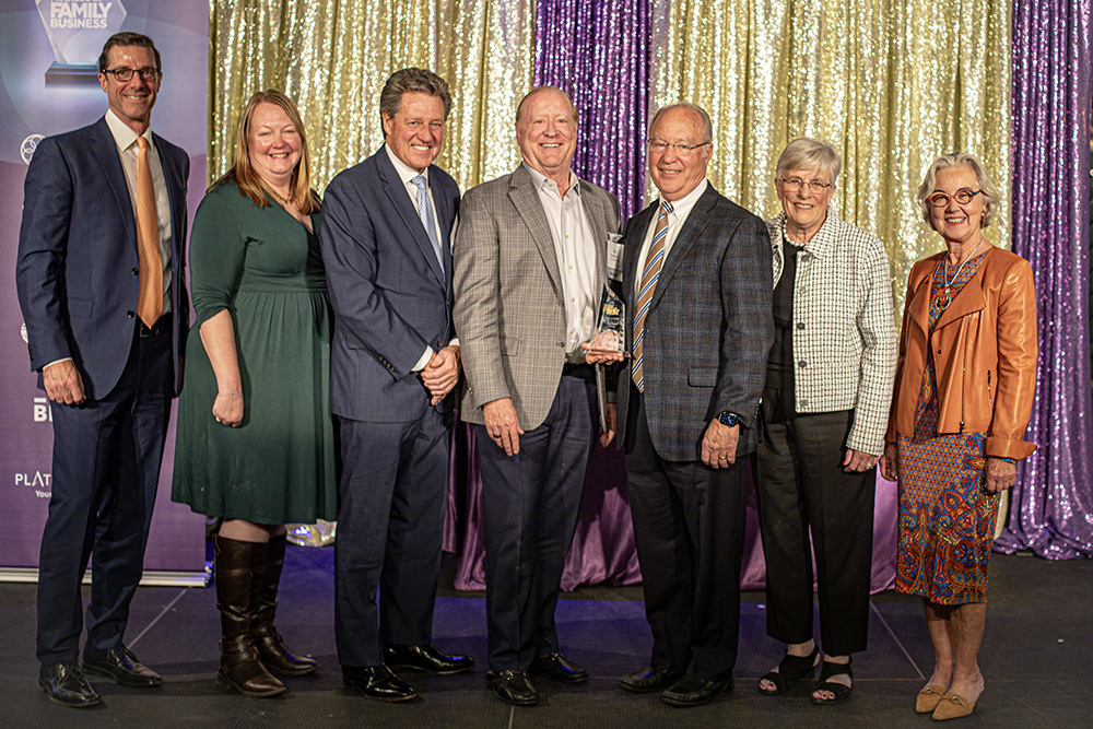 group of people standing on a stage with a man in the center holding an award