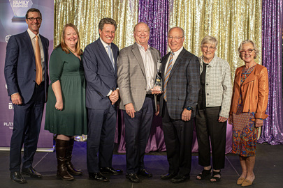 group of people standing on a stage with a man in the center holding an award