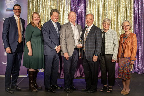 group of people standing on a stage with a man in the center holding an award