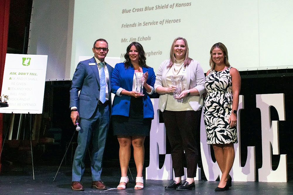 group of people standing on a stage with a woman holding an award