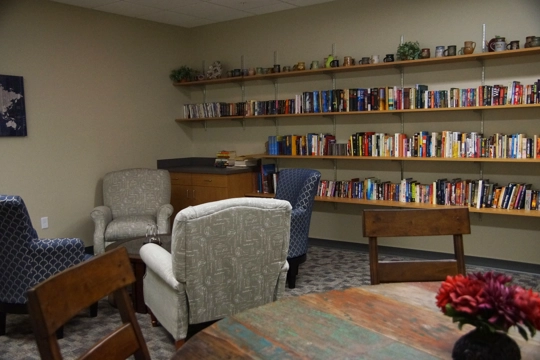 room with seating areas in foreground and shelves of books along wall in background