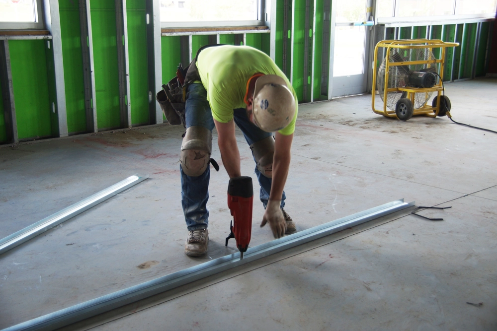 man using nail gun inside building under construction