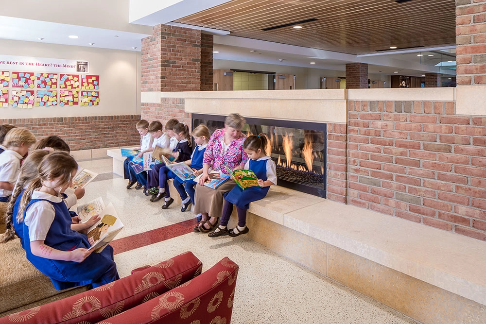 young private school children and their teacher read in front of a fireplace