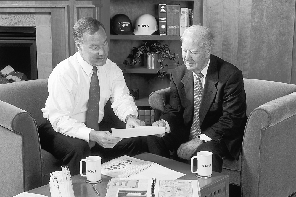 black and white photo of two men in professional attire seated and looking at a document