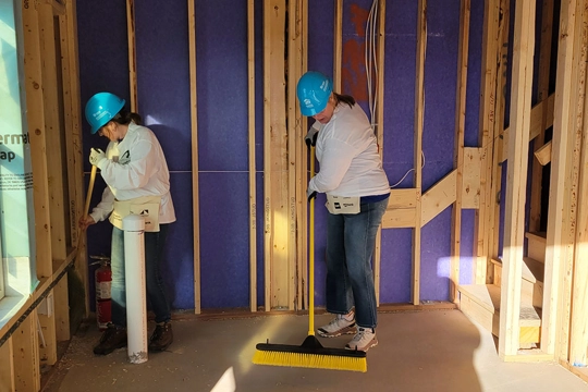 two people sweep a floor in the unfinished room of a home