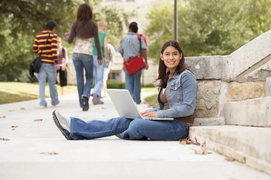 woman sitting outside on sidewalk with laptop computer