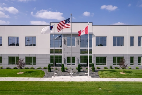 front glass entrance to a two-story building with three flags in the foreground