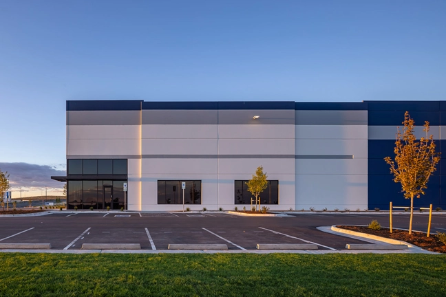 Front entrance of a speculative industrial building lit up at dusk with custom building lighting and the setting sun