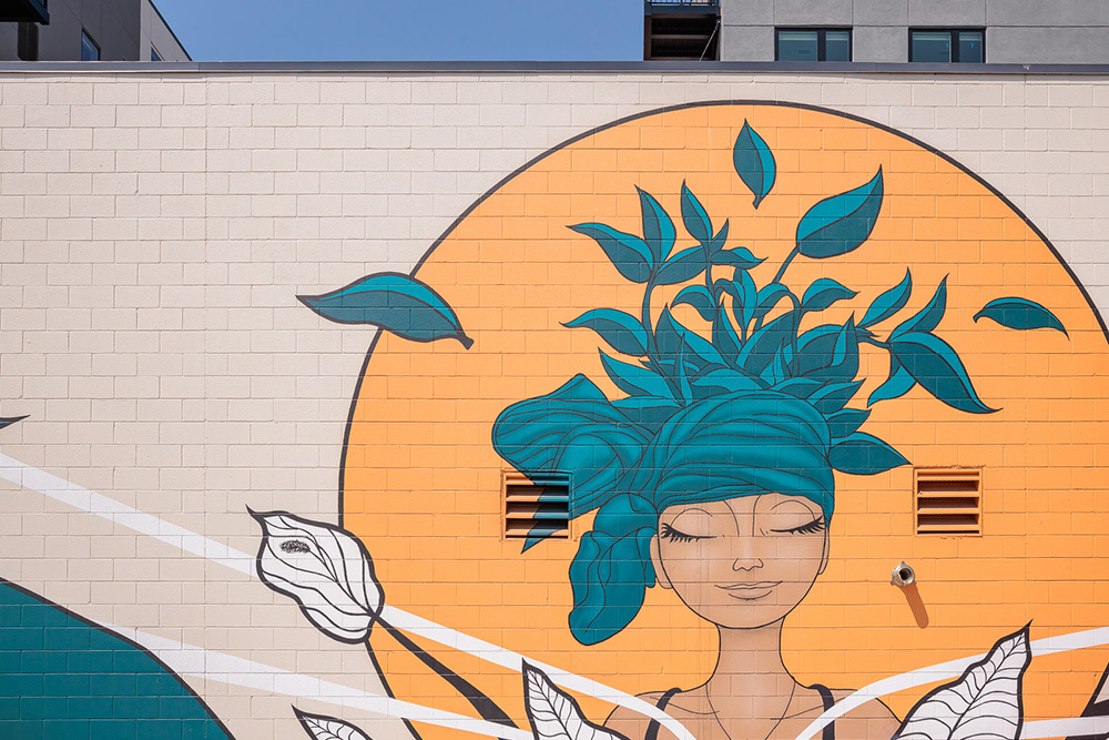 Mural of woman with hair of leaves on parking garage of multifamily development