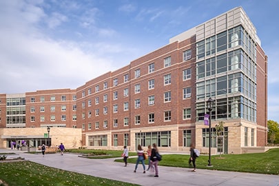 Young people walk on a sidewalk in front of a new multistory university building.