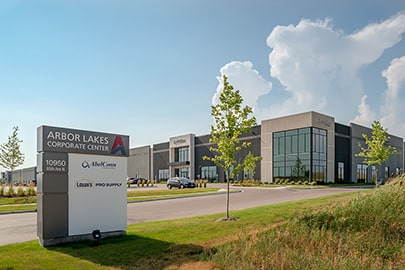 A monument sign sits in front of a large, nicely designed industrial building with trees and grass.