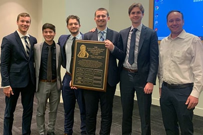 6 young men in professional attire stand in a line with one holding a large plaque.