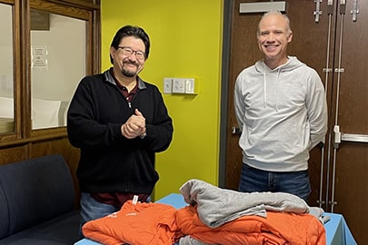 Two smiling man stand behind a table with stacks of folded t-shirts.