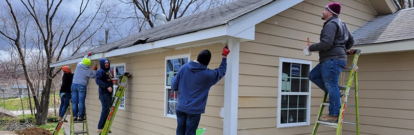 Five people on ladders and step stools paint a house for Habitat for Humanity.