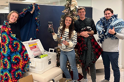 Two smiling women and 2 smiling men with fleece blankets and socks to be donated.