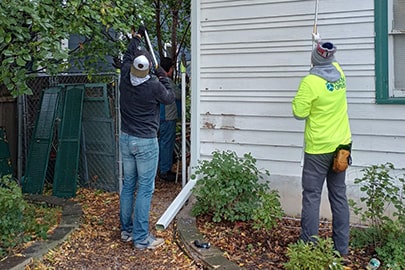 Two people with their backs to the viewer paint the exterior of a house.