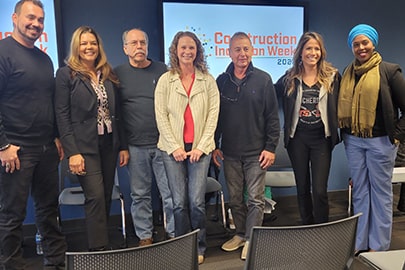 A group of smiling people post for a photo in front of a monitor screen that says Construction Inclusion Week.