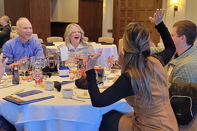 A man and a woman at a table react excitedly to a man and woman sitting across the table from them.